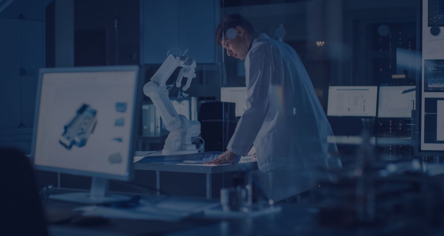 A man in a lab coat in front of computer screens and robot arms